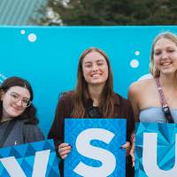 three students posing in front of backdrop at Laker Kickoff photo booth holding GVSU letters